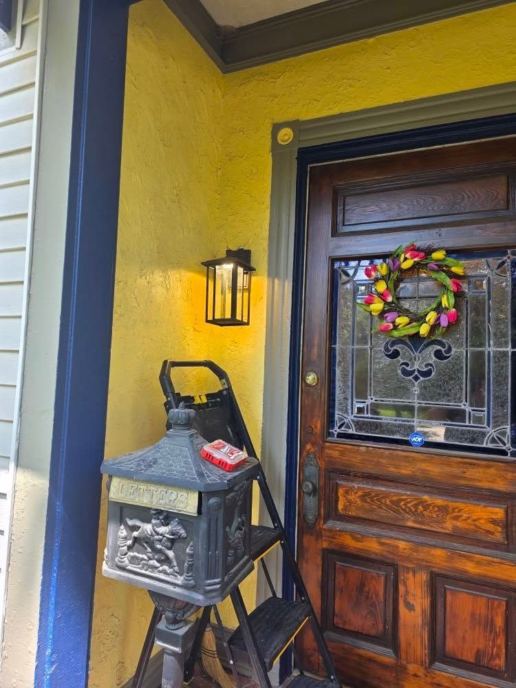 Black lantern beside a yellow wall, brown door with a stained glass window, and a wreath.