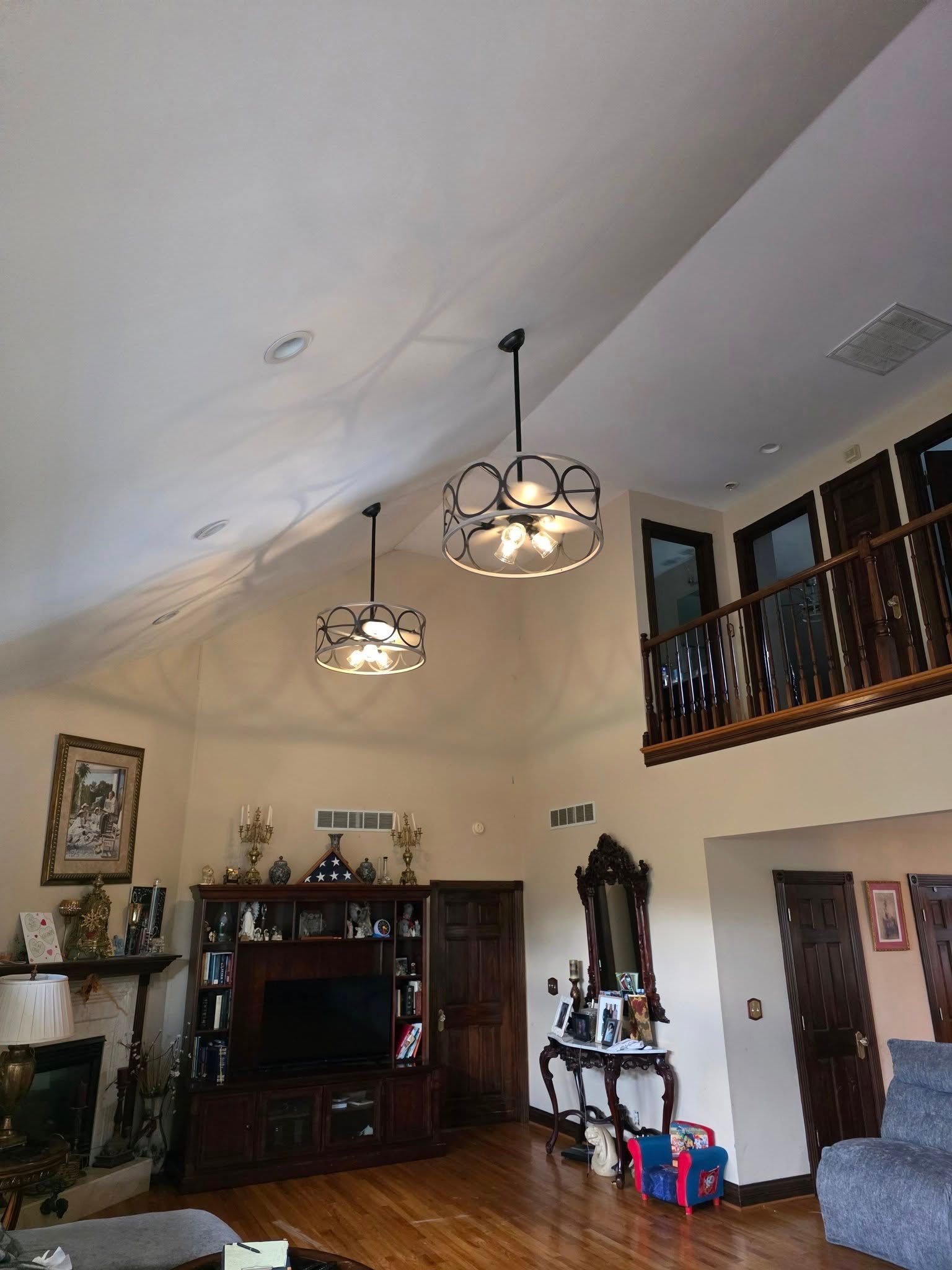 High-ceiling living room with two decorative light fixtures, a balcony, and built-in entertainment center.