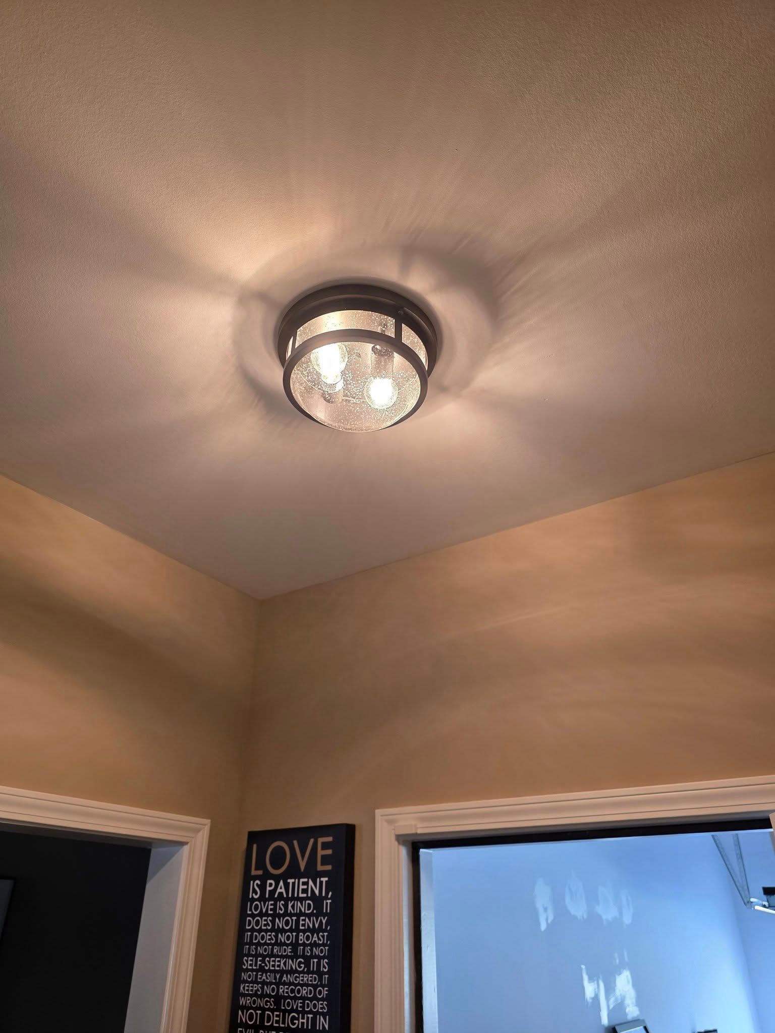 Ceiling light fixture illuminating a room with tan walls and a dark framed sign.