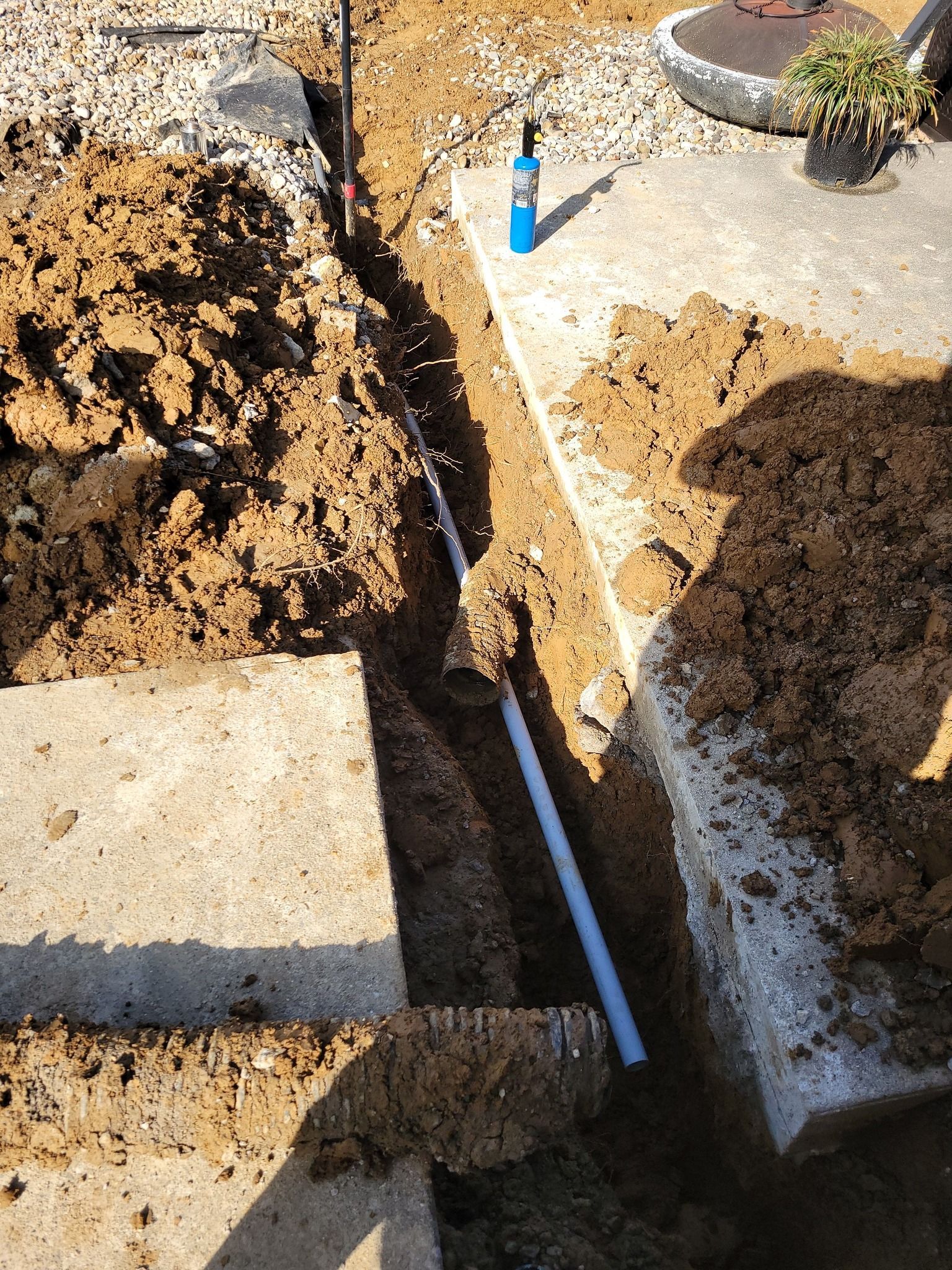 Trench dug in dirt, with buried water pipes visible. A concrete structure is on the left and upper right of the trench.