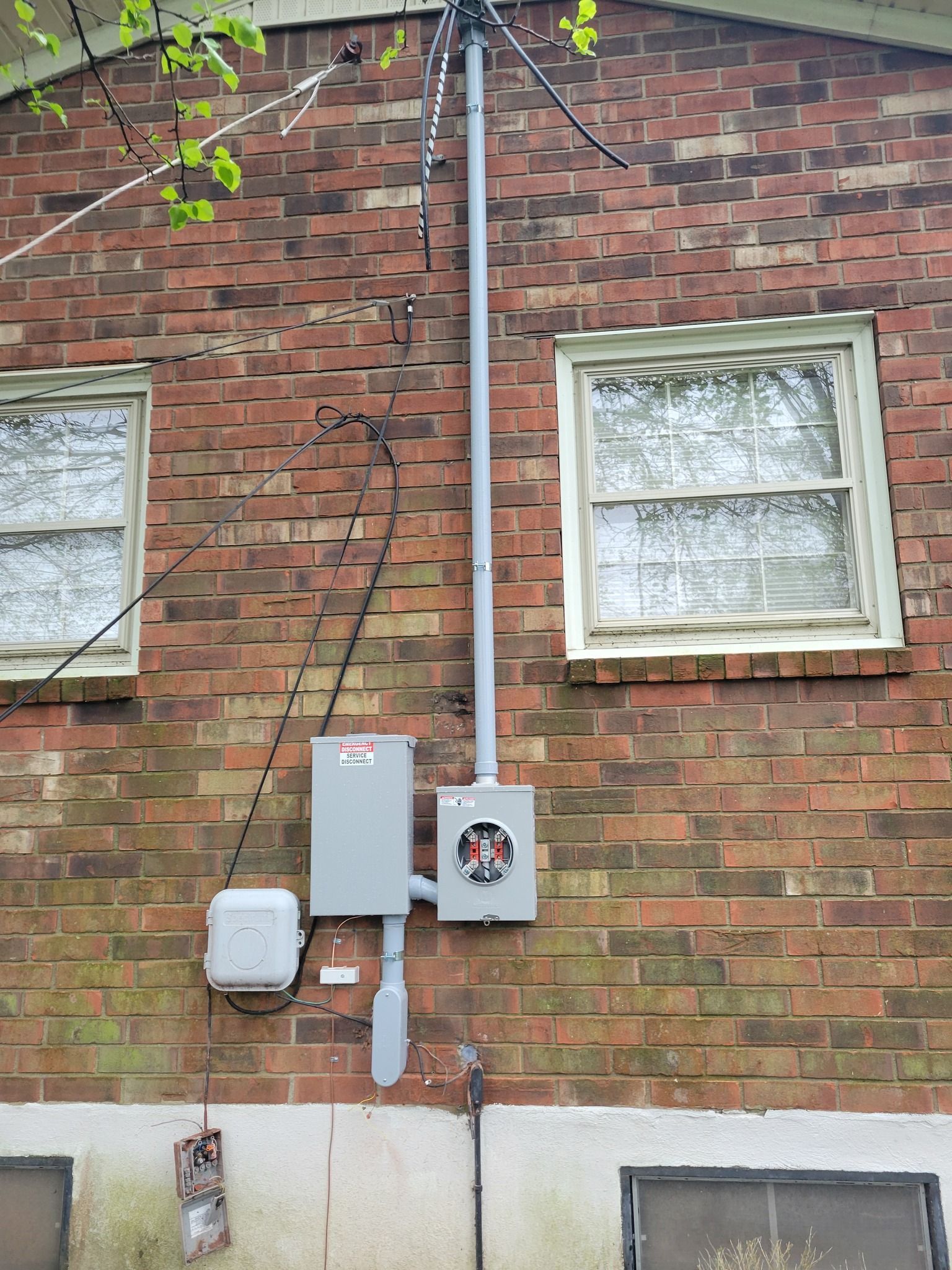 Exterior wall with electrical meter, conduit, junction boxes, and windows on a brick building.