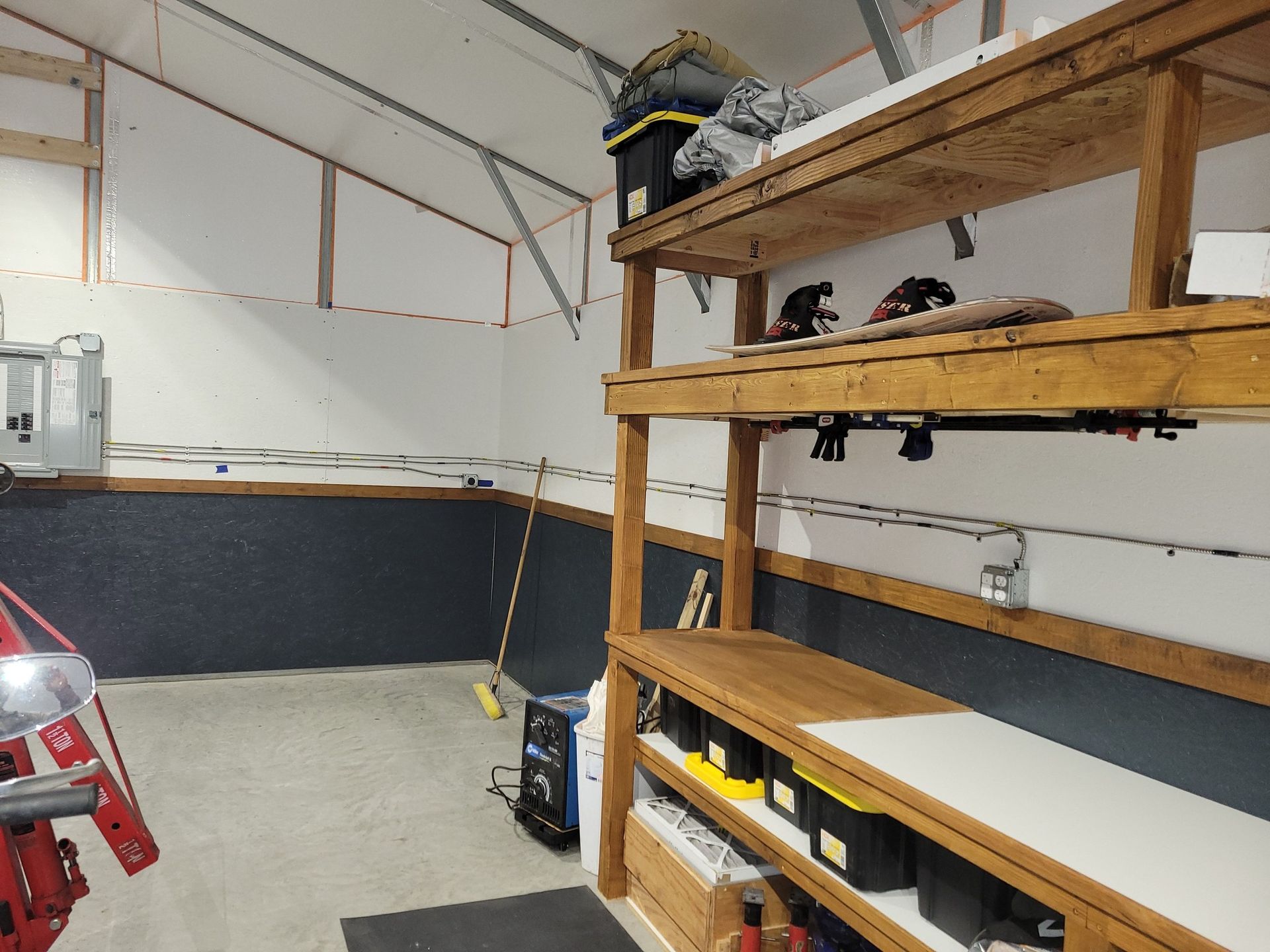Garage interior with wooden shelves, black storage bins, and tools.