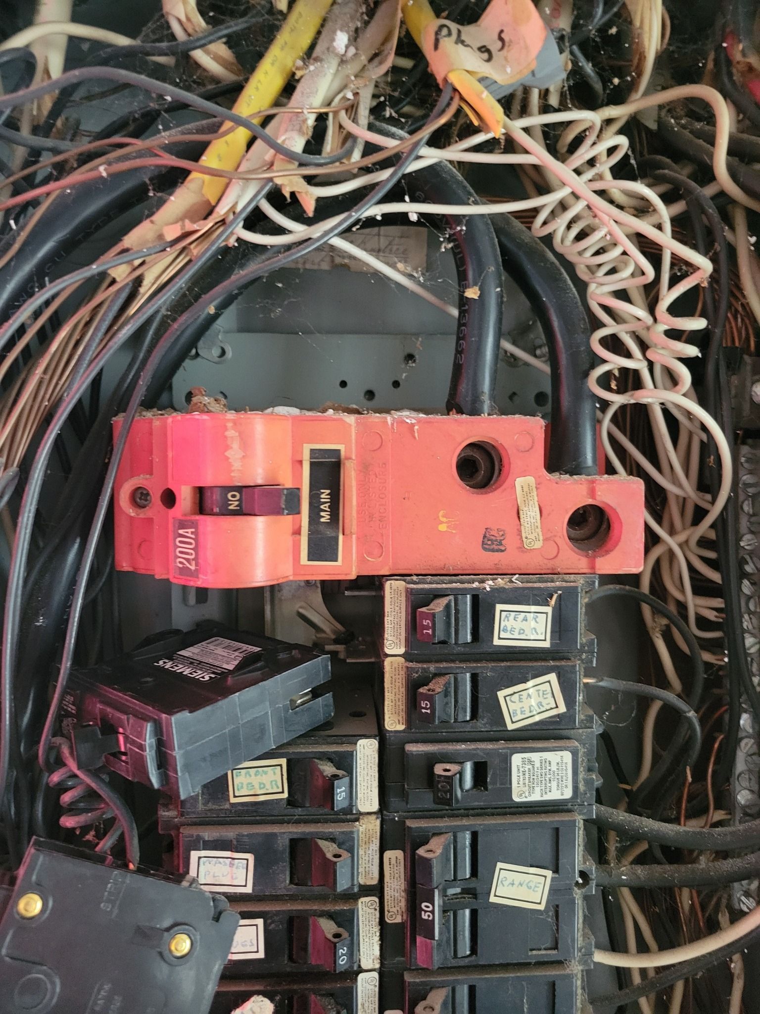 Electrical panel with orange main breaker and numerous circuit breakers. Wires are tangled.