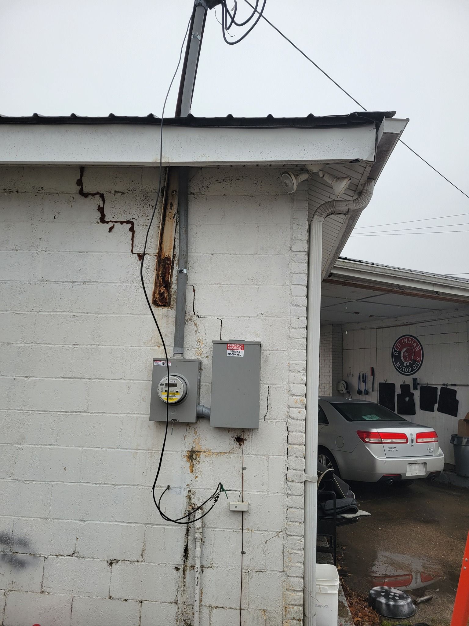 Electrical meter and panel mounted on a white brick building exterior. A car is parked nearby.