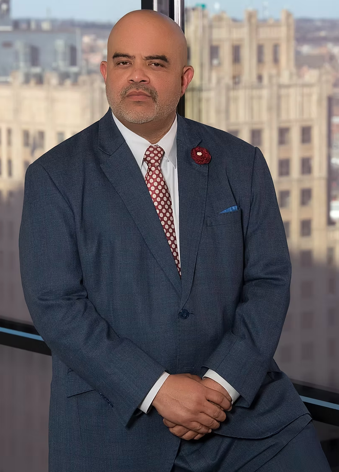 A man in a suit and tie is standing in front of a window.