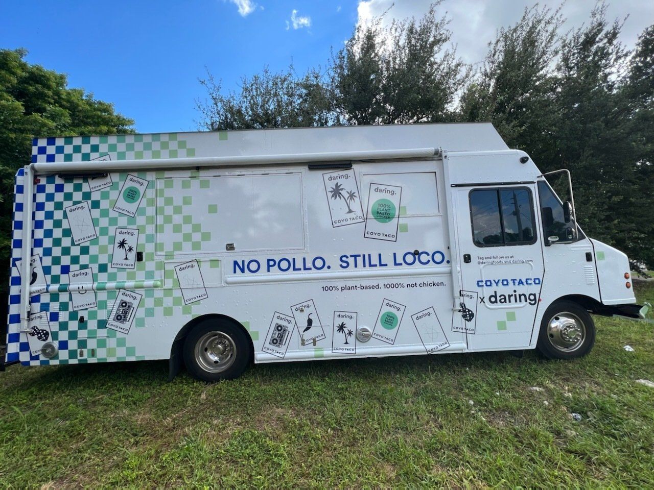 A white food truck is parked in a grassy field.
