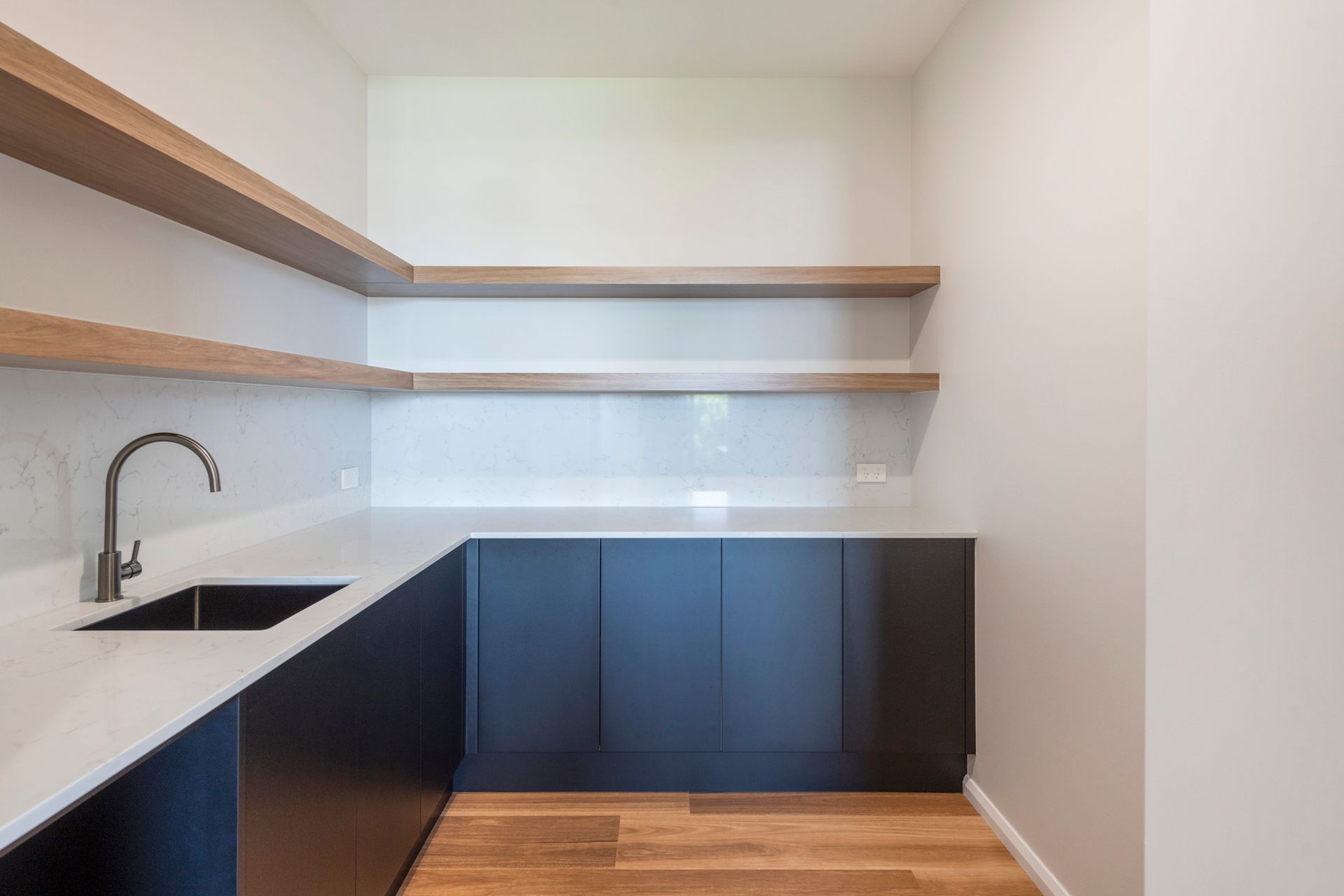 Modern butler's pantry with black cabinets, white countertops, floating shelves, and a sink.