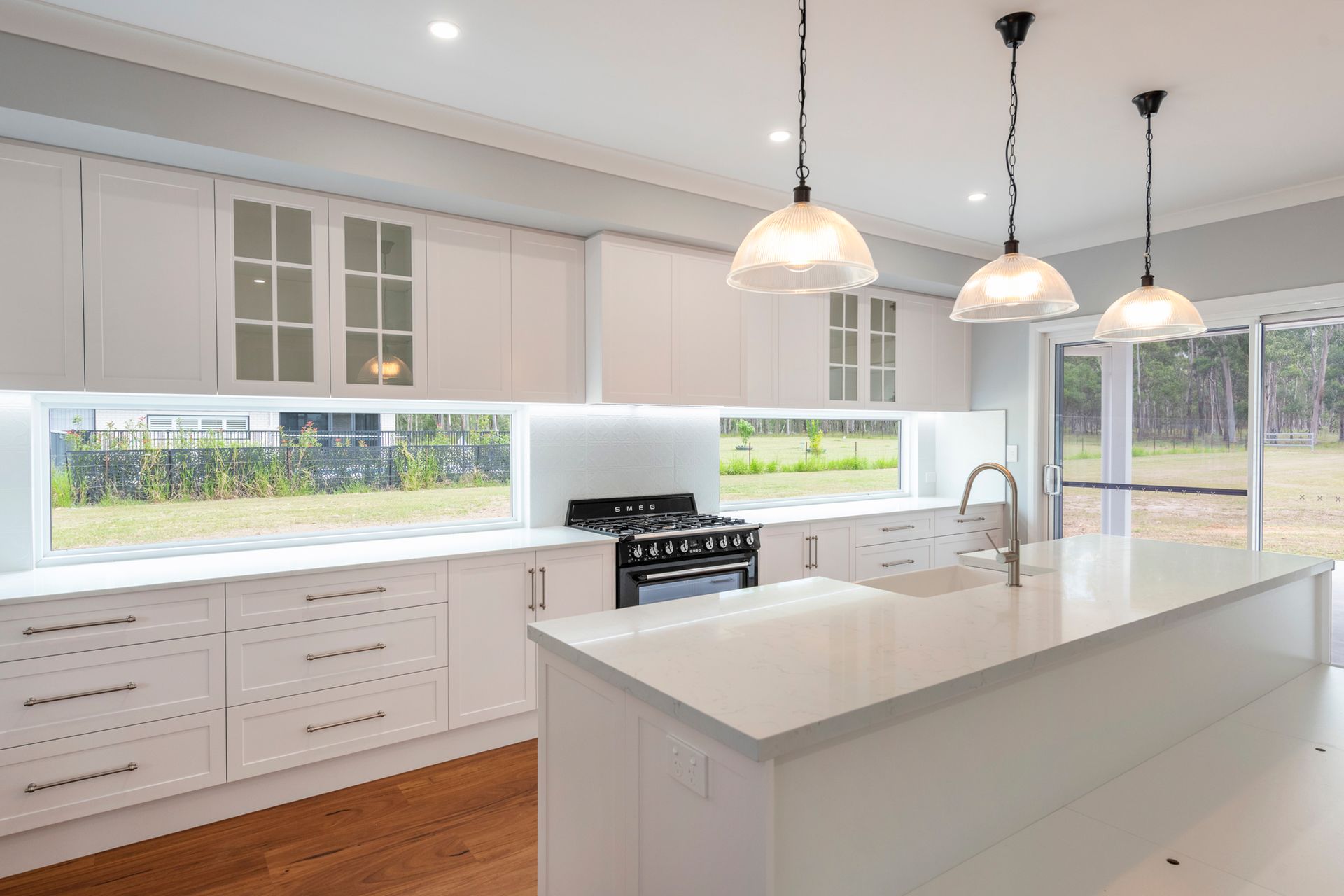Bright white kitchen with island, glass-fronted cabinets, a range, and three pendant lights.