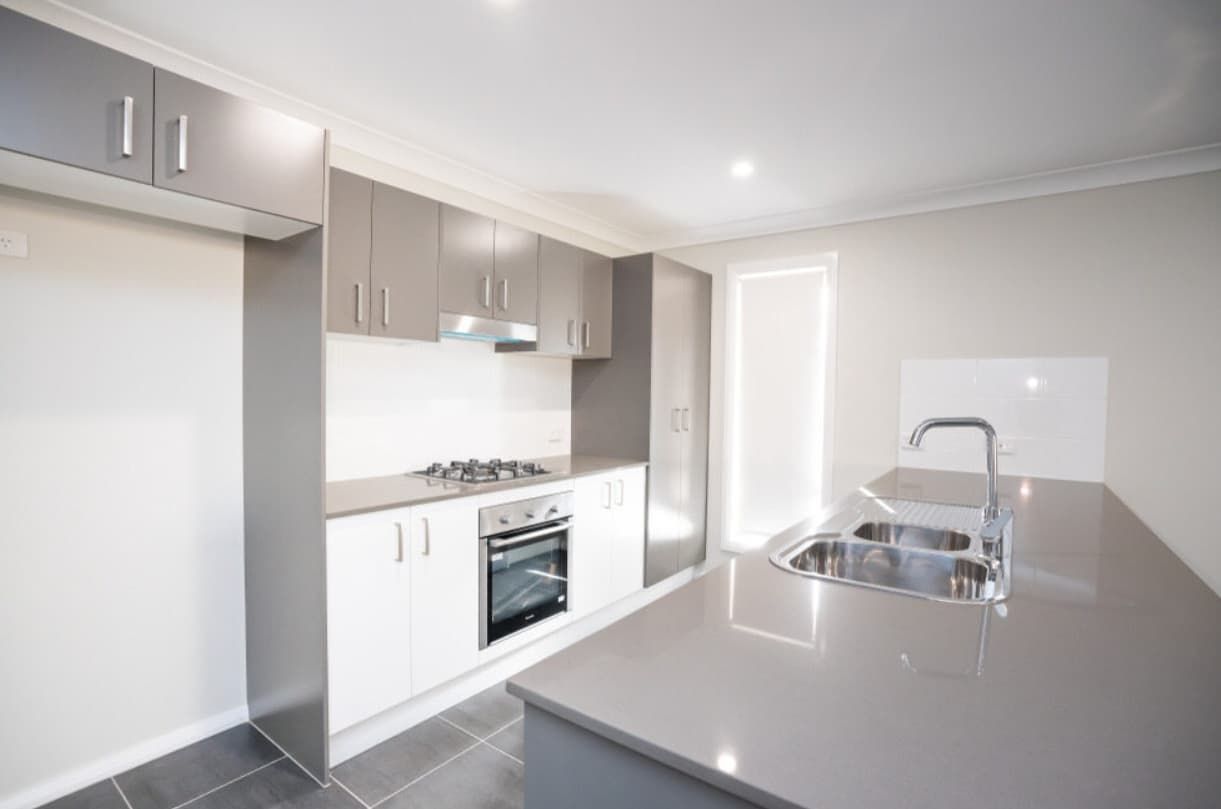 An Empty Kitchen With White Cabinets , A Sink , And A Stove — Content Stone In Lismore, NSW