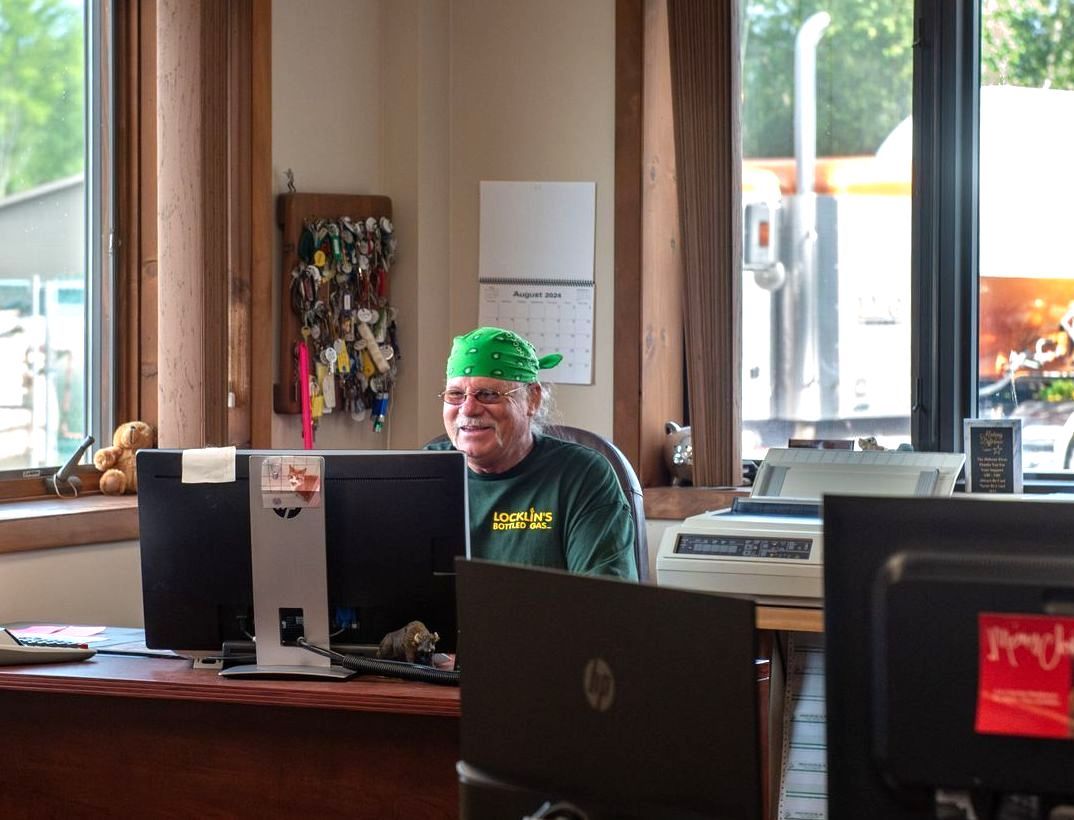 A man wearing a green hat is sitting at a desk in front of a computer.