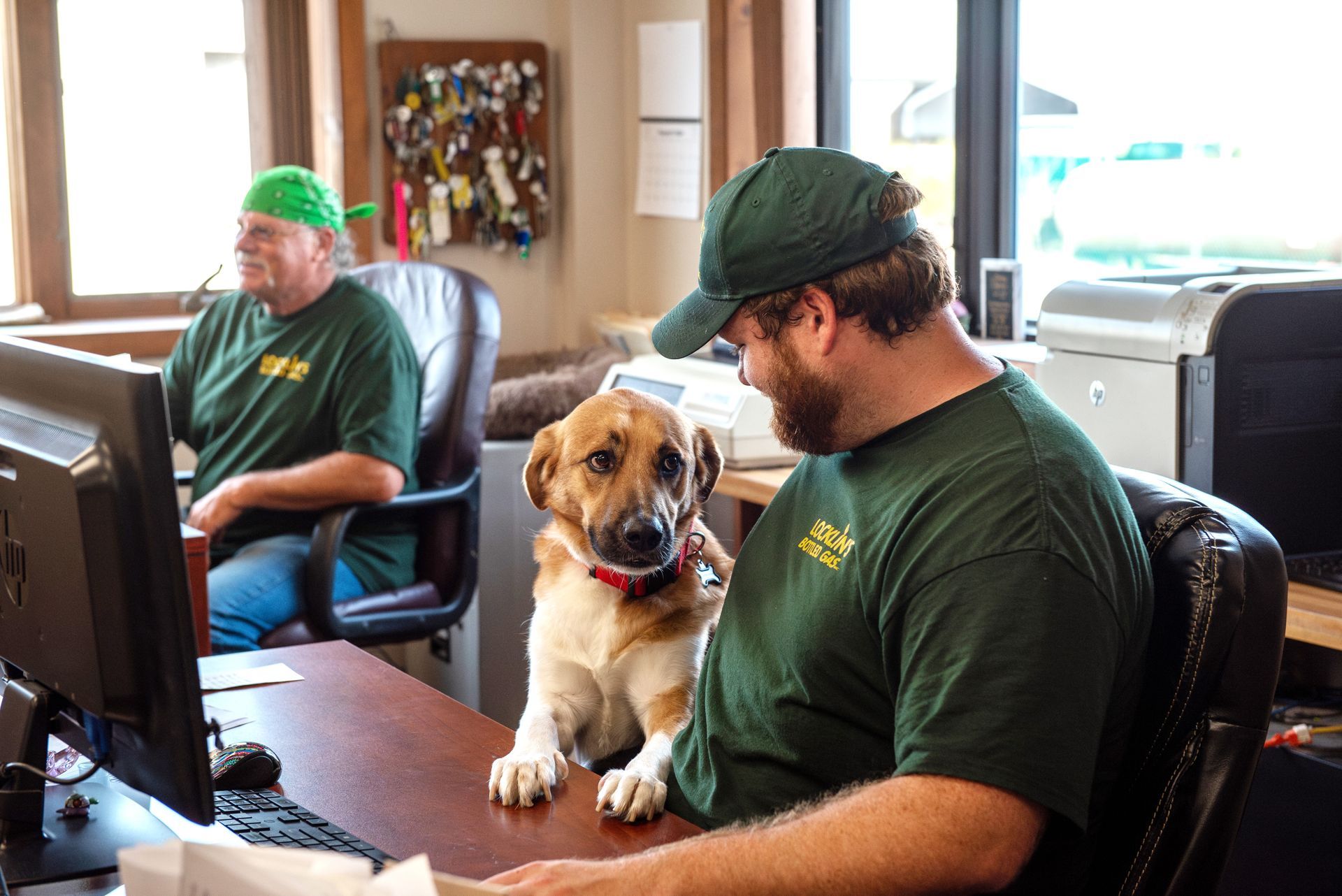 A man and a dog are sitting at a desk in front of a computer.