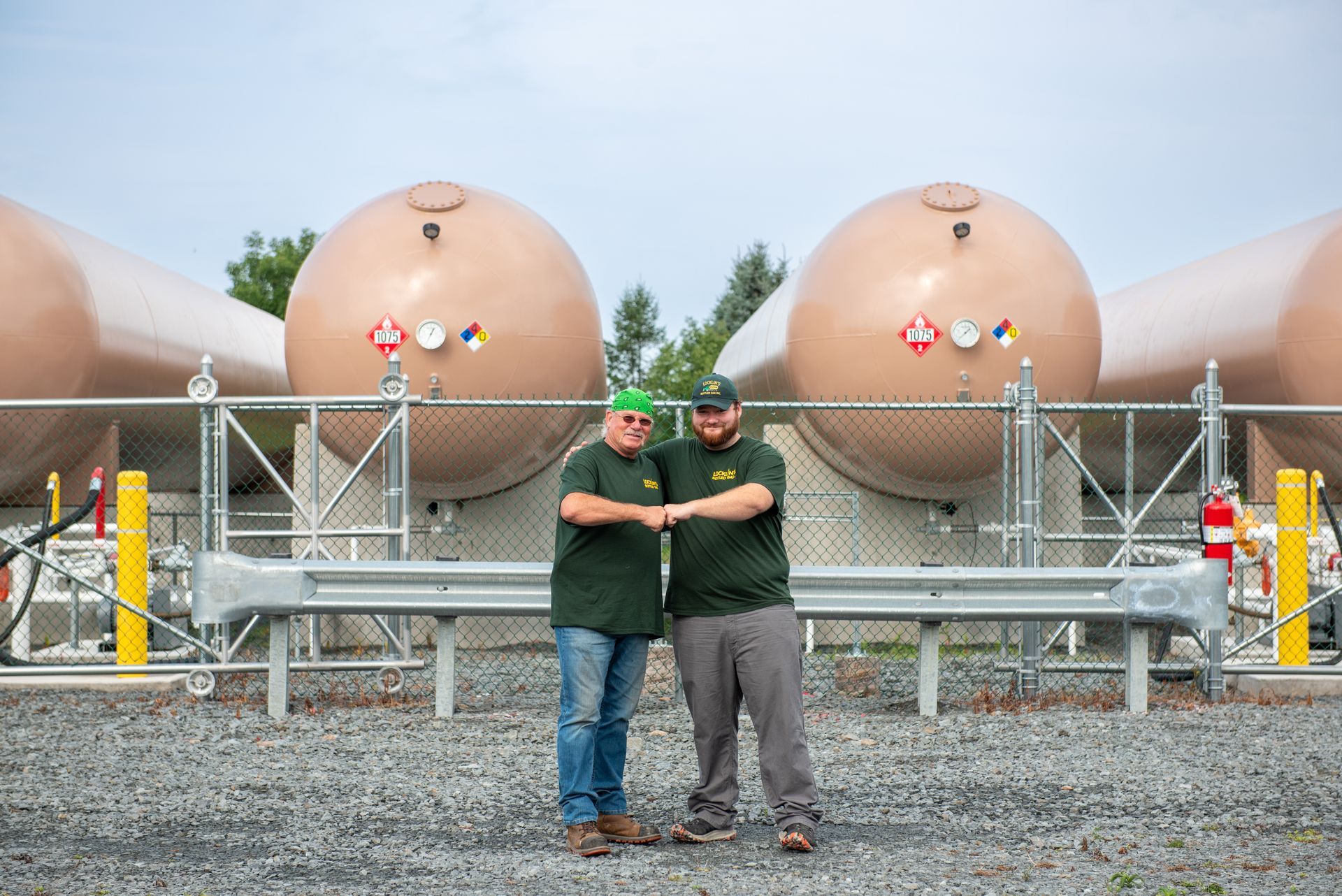 Two men are shaking hands in front of a row of large tanks.