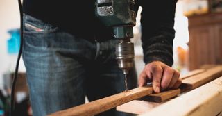 A man is using a drill to drill a hole in a piece of wood.