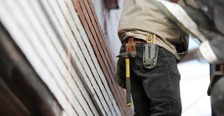 A man is carrying a hammer and a tape measure around his waist.