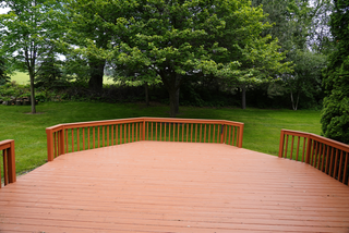 An empty wooden deck with a wooden railing and trees in the background.