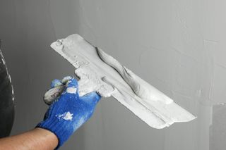 A person is plastering a wall with a trowel.