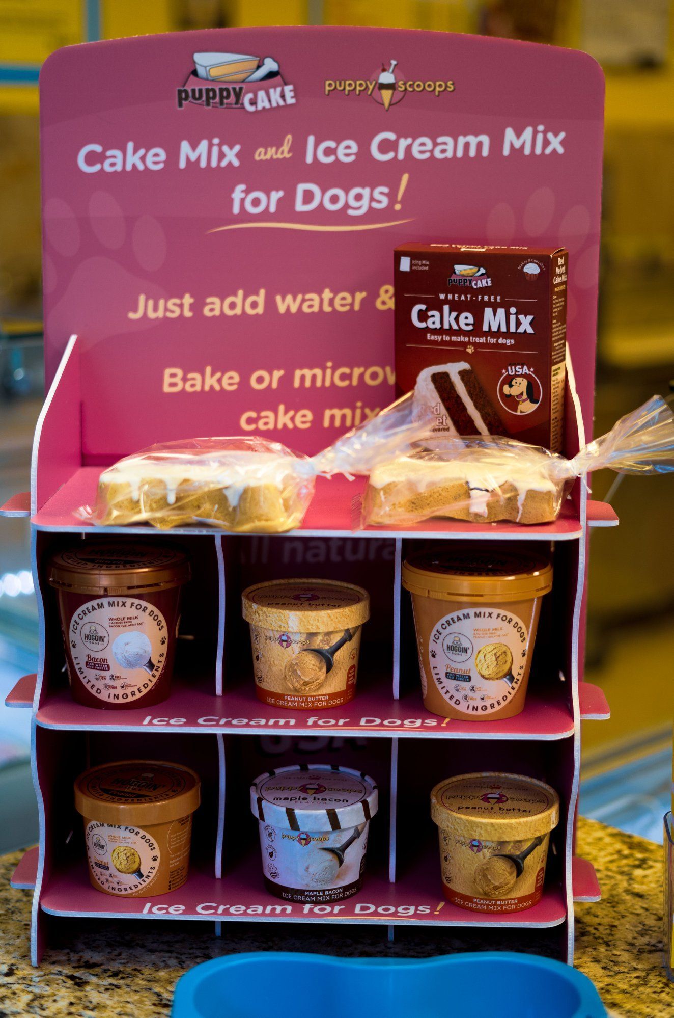 Display of dog cake and ice cream mixes. Includes products and baked goods on a pink shelf.