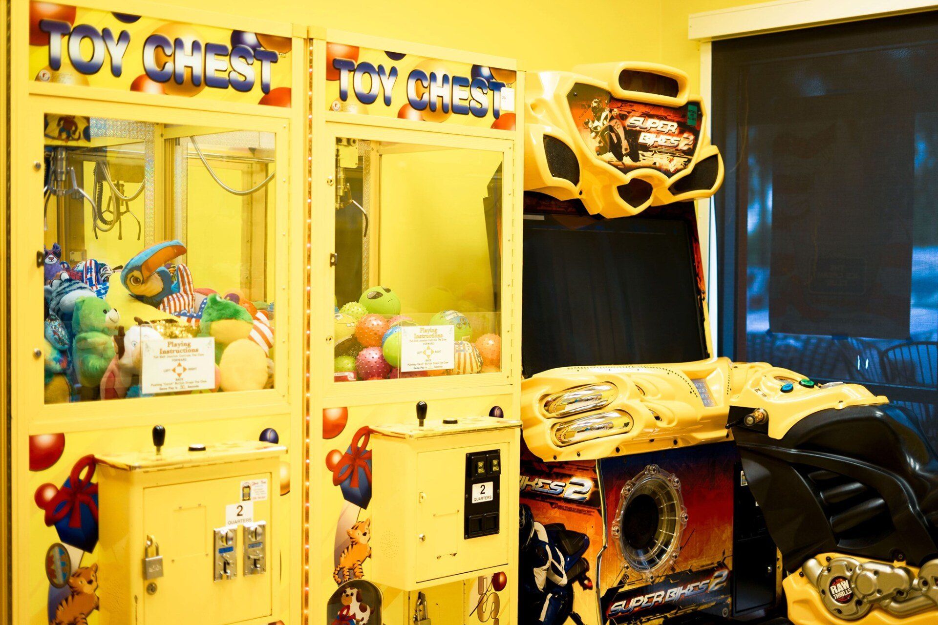 Two yellow claw machines and a racing arcade game in a room.