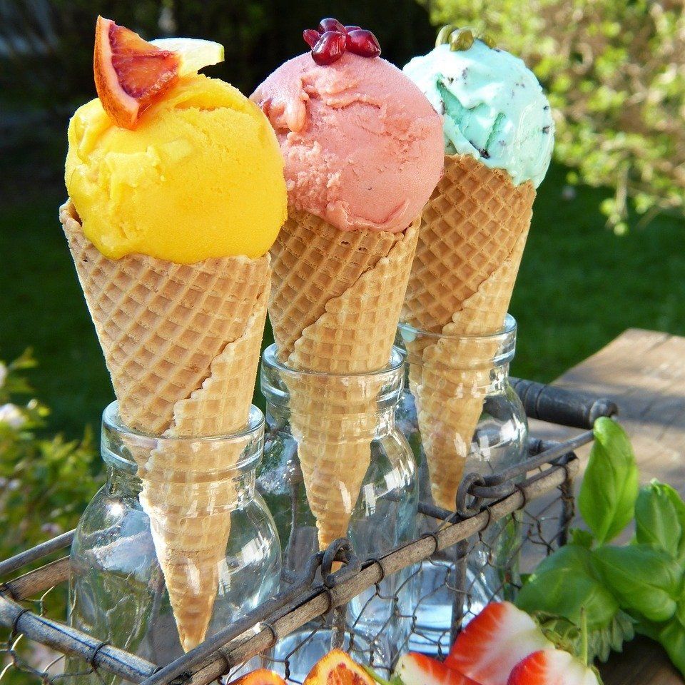 Three ice cream cones in different colors: yellow, pink, and green, sitting in glass jars.