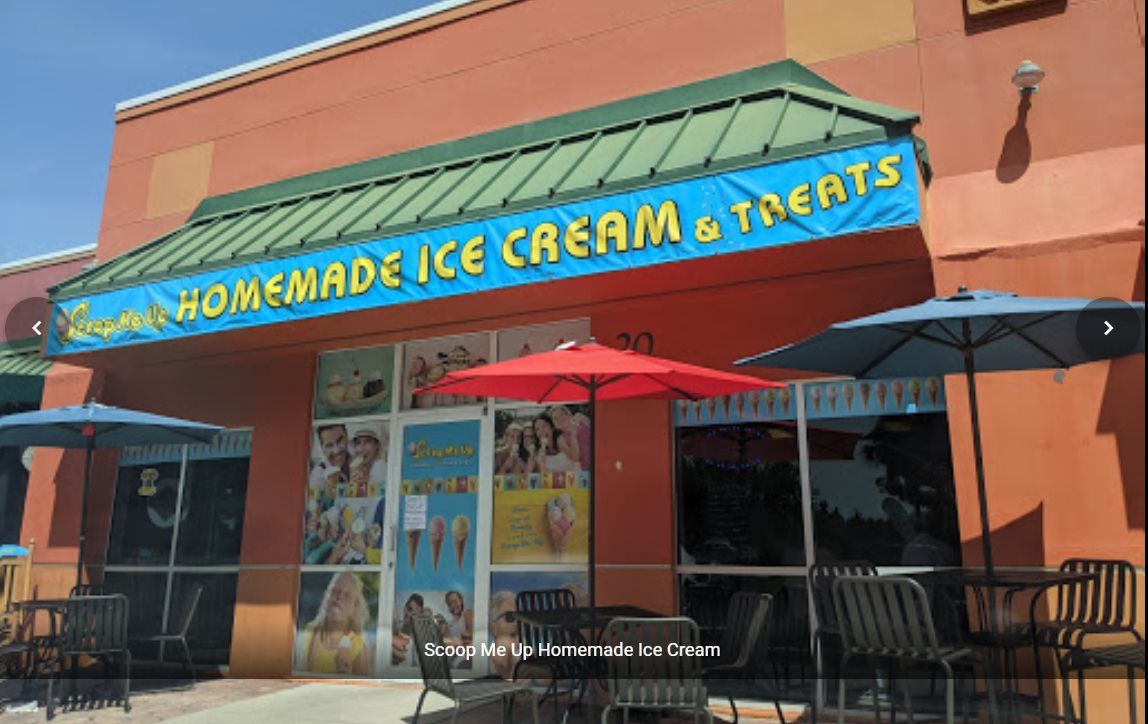 Exterior of ice cream shop: Orange building with blue awning, tables and umbrellas.