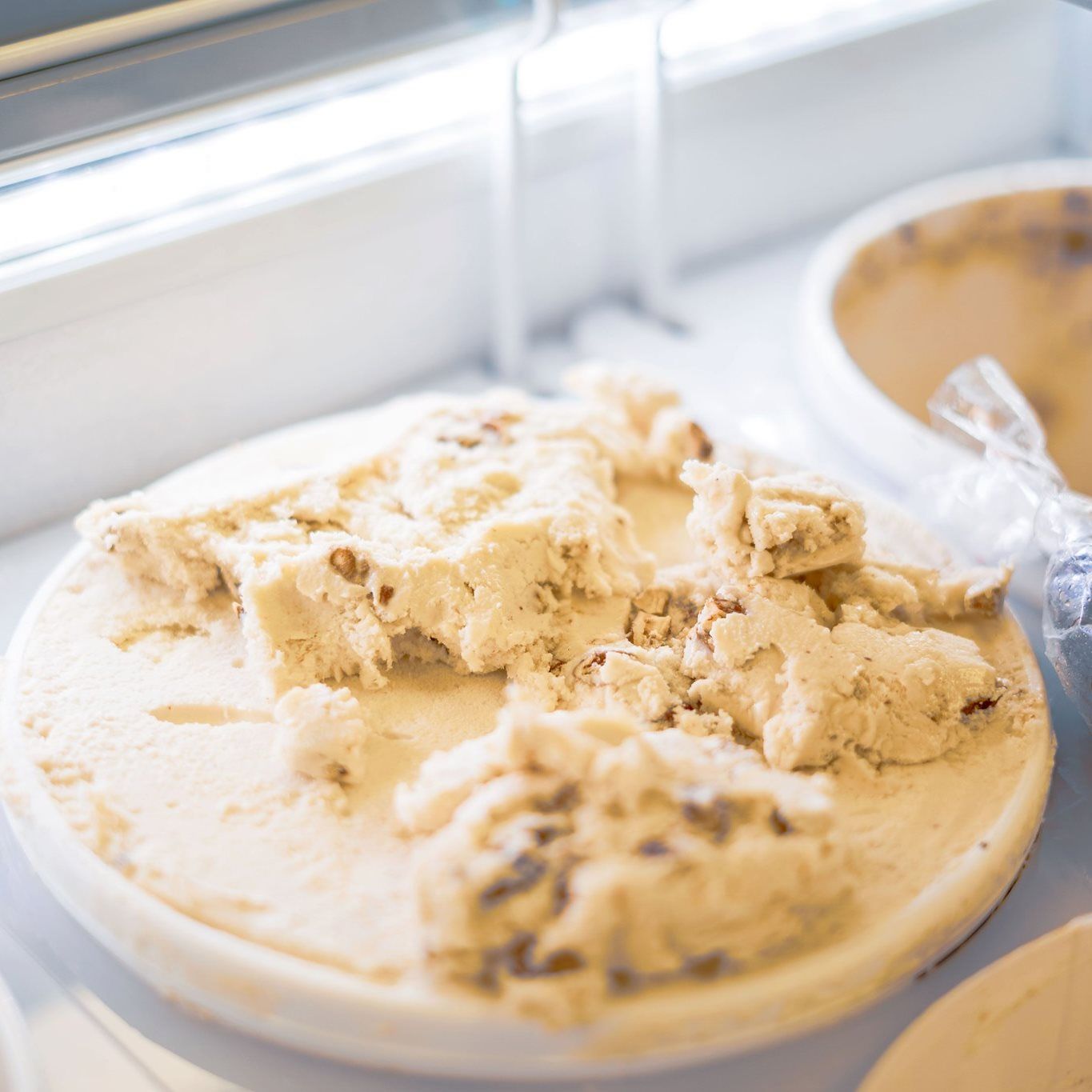 A white plate holds scoops of light brown, nutty fudge with pieces broken off.