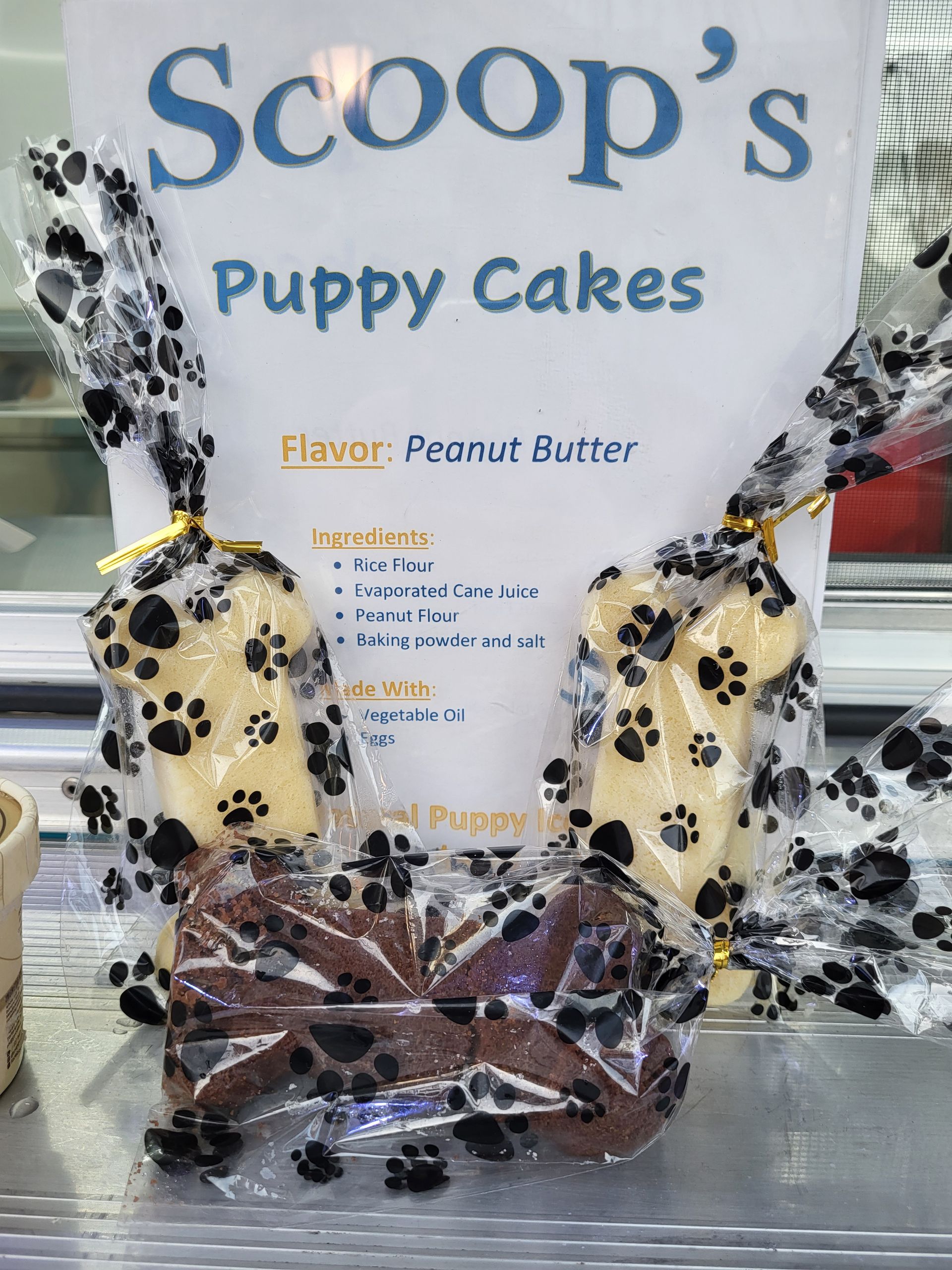 Dog treats: peanut butter-flavored puppy cakes in bone shapes, packaged in paw print bags, behind a display sign.
