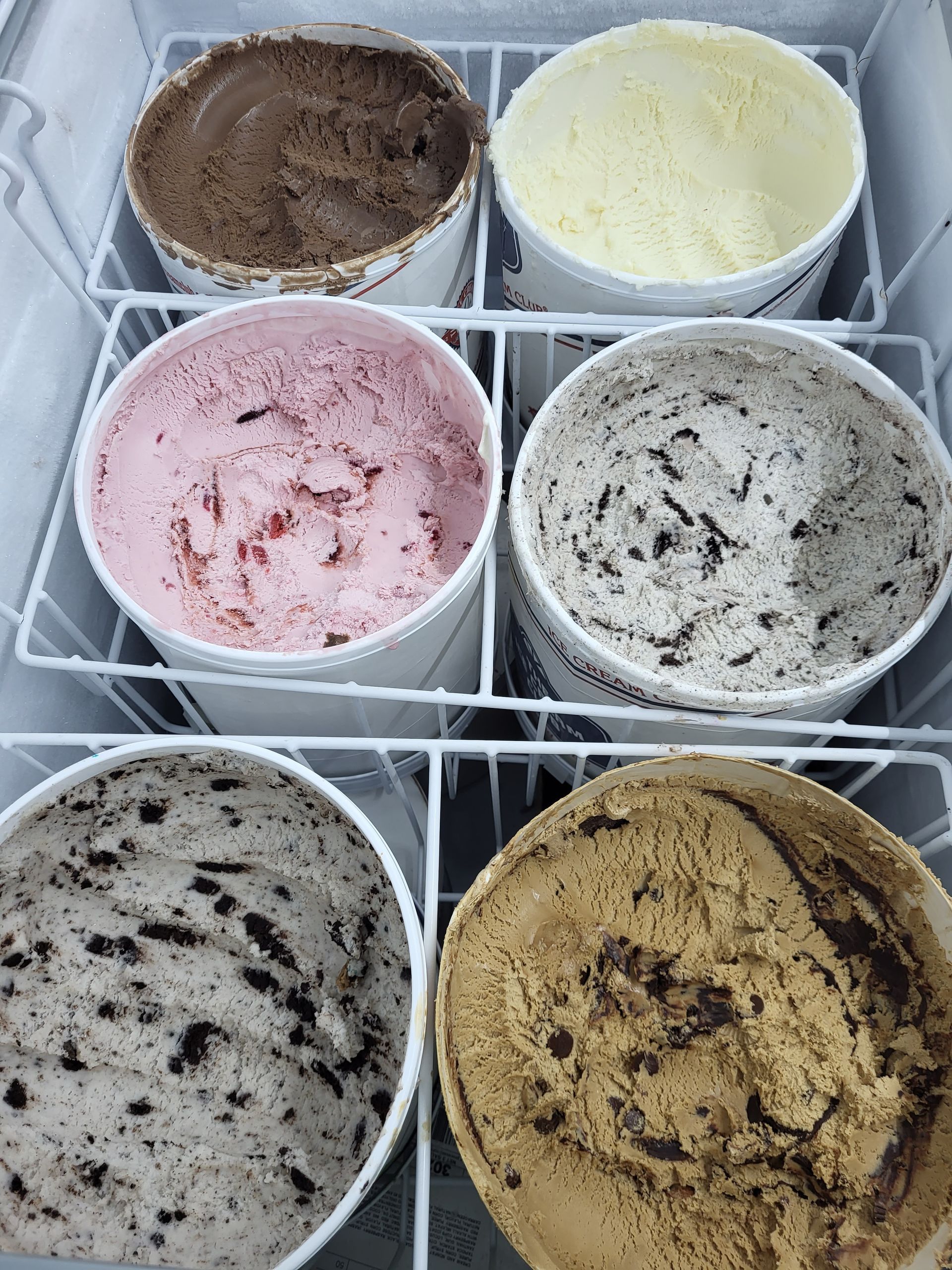 Six tubs of ice cream in a freezer. Flavors include chocolate, vanilla, strawberry, cookies and cream, and coffee.