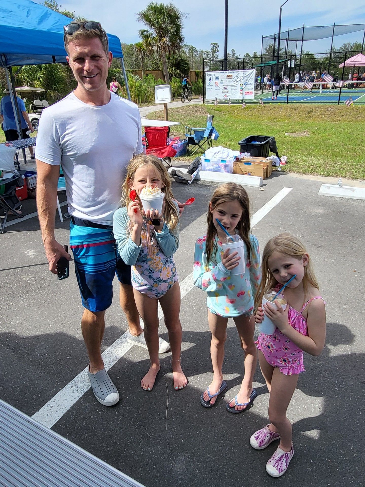 Man and three girls in swimsuits with blue faces holding frozen treats outdoors.