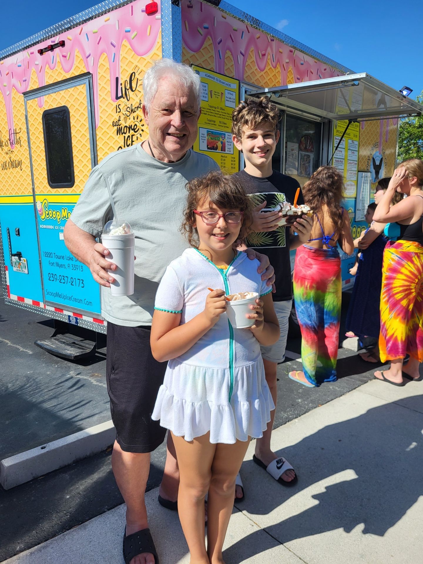 Man and two children smiling with ice cream, near a colorful food truck outdoors.