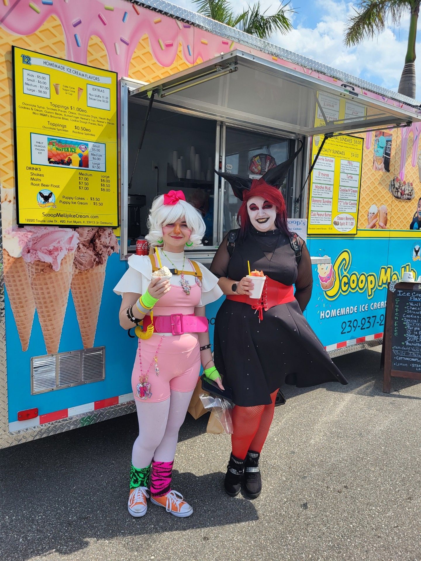 Two cosplayers in front of an ice cream truck. One in pink, the other in red and black.