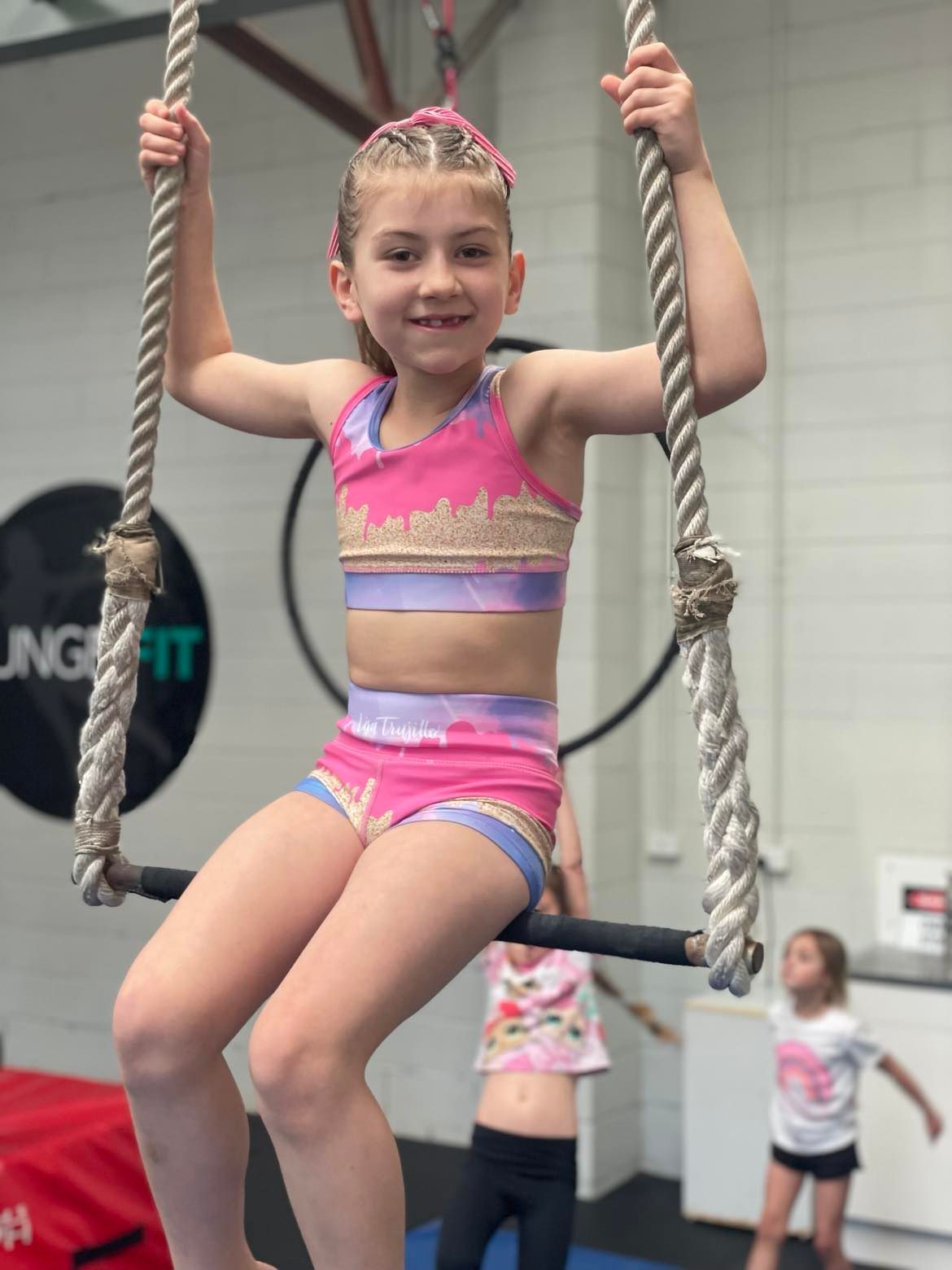 A young girl is sitting on a rope swing in a gym