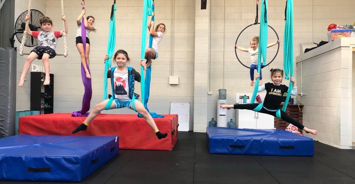 A group of children are doing aerial acrobatics in a gym.