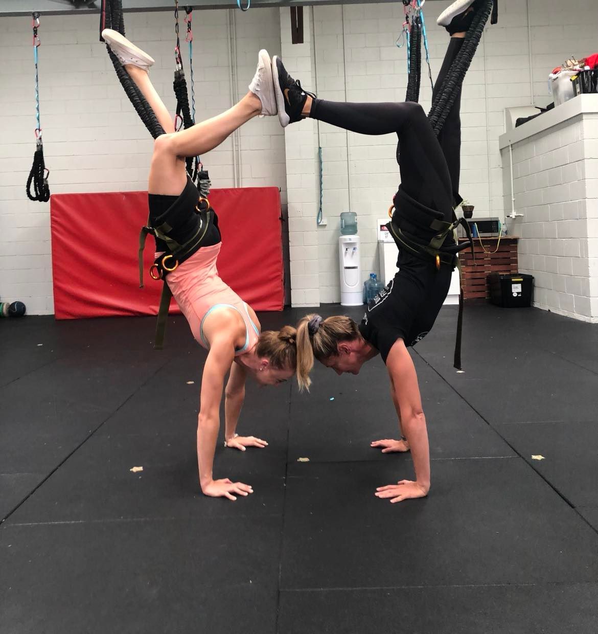 Two women are doing handstands in a gym