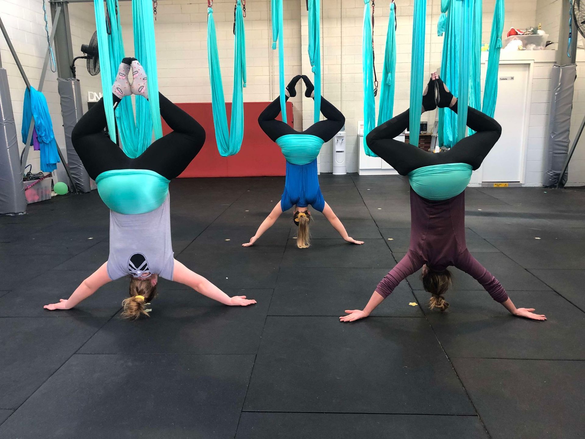 Three women are doing aerial yoga in a gym