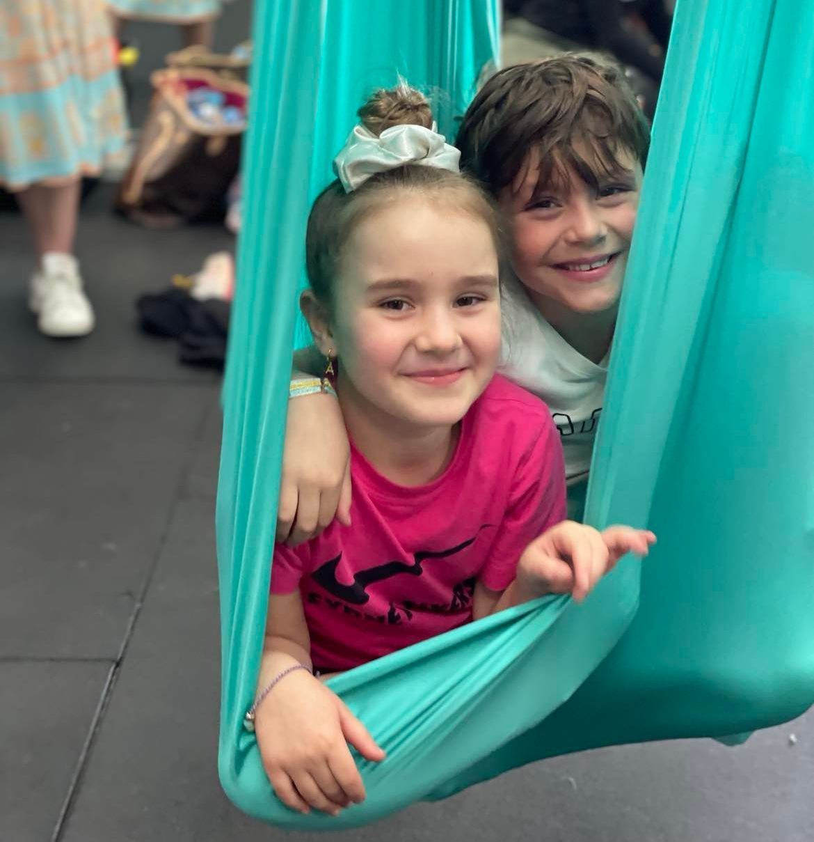 A boy and a girl are sitting in an aerial hammock.