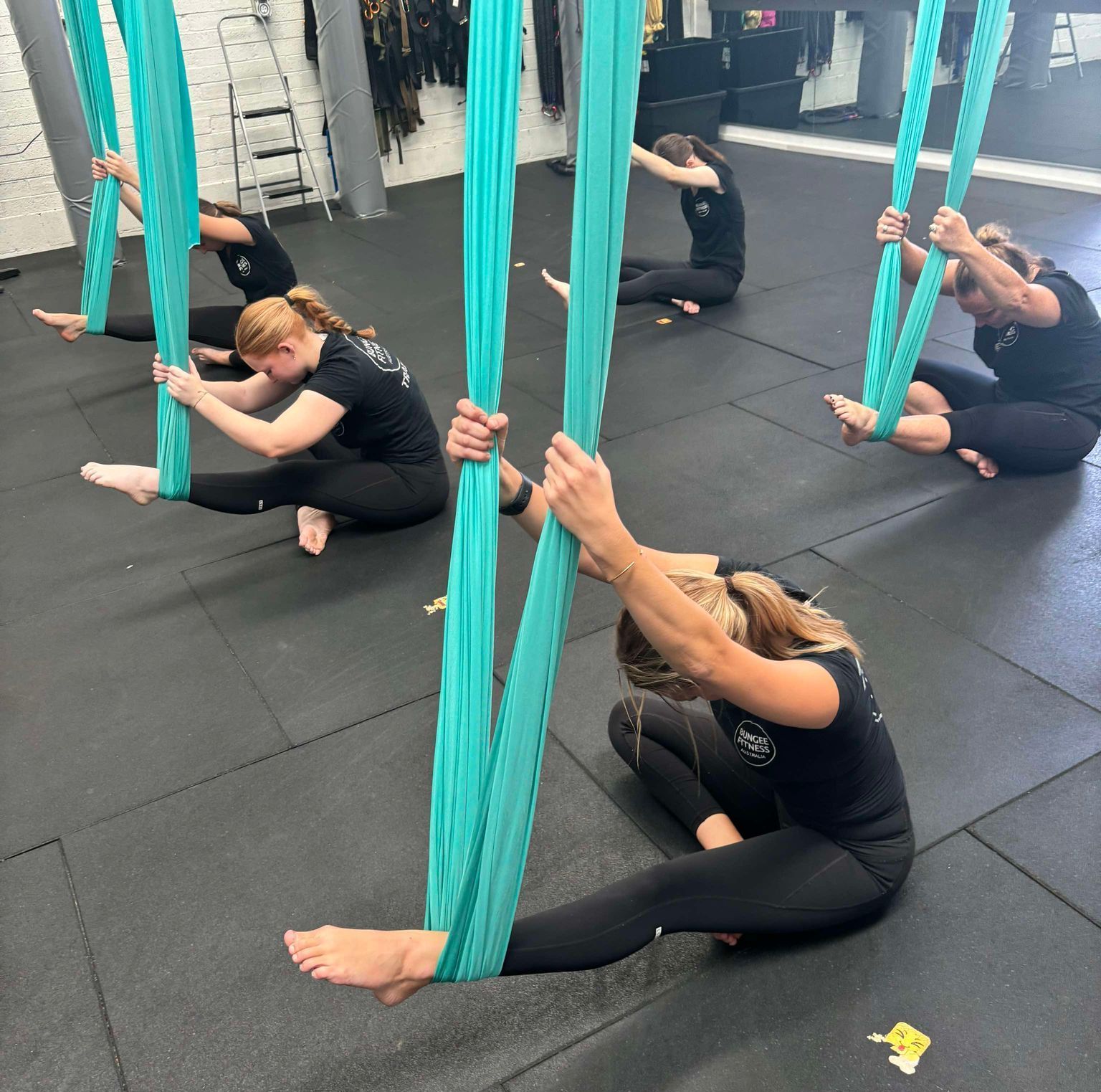 A group of people are doing aerial yoga in a gym