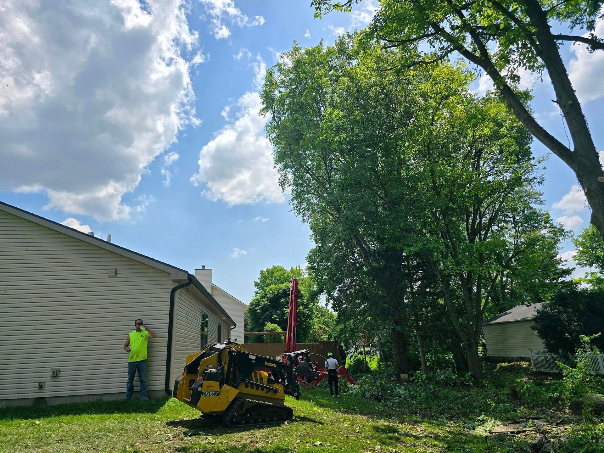 A man is standing in front of a house next to a tree stump grinder.