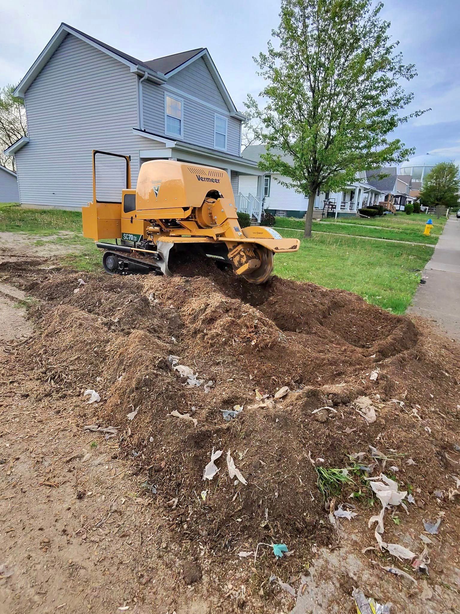 A stump grinder is sitting on top of a pile of dirt in front of a house.