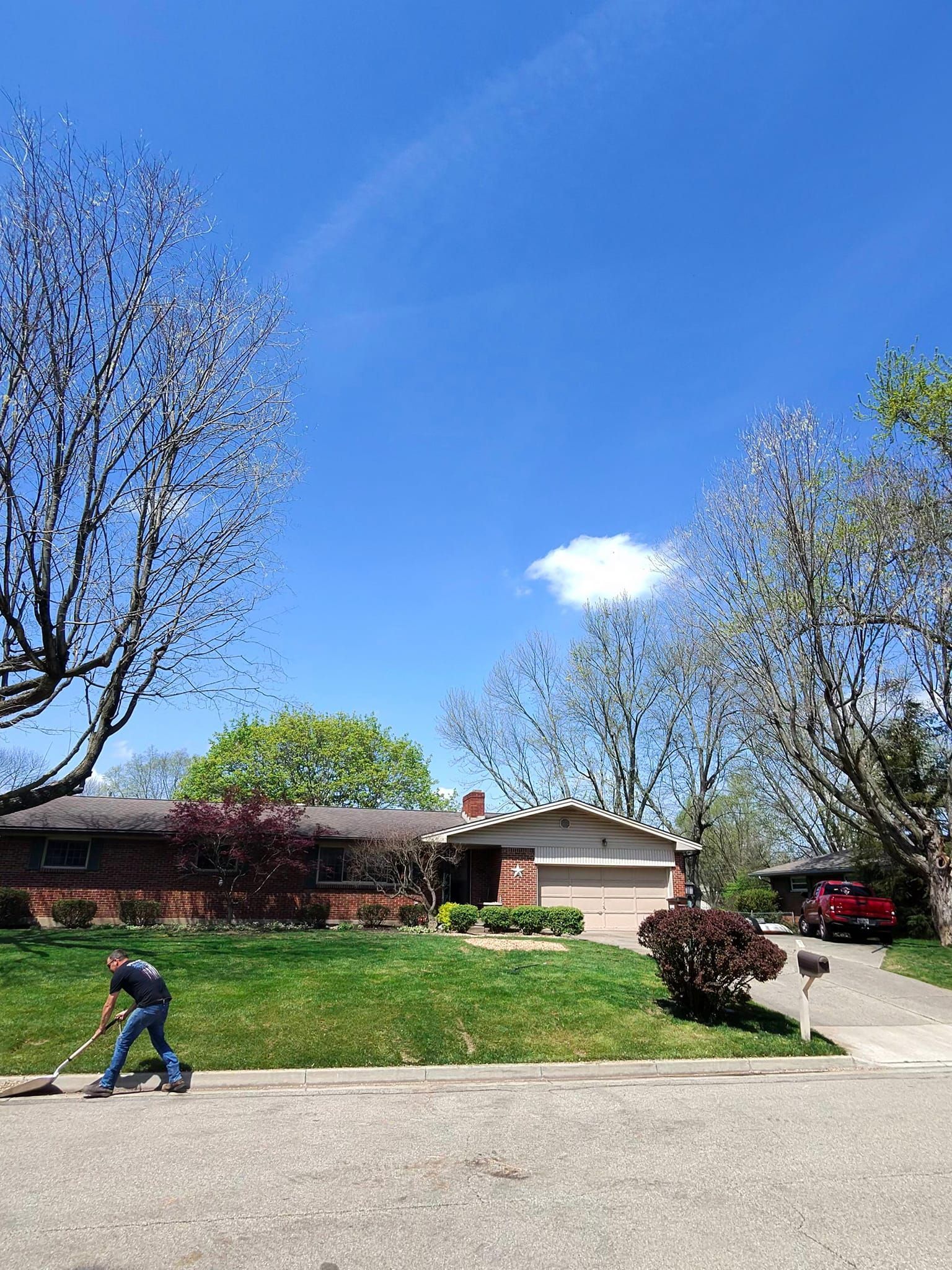 A man is sweeping the grass in front of a house on a sunny day.