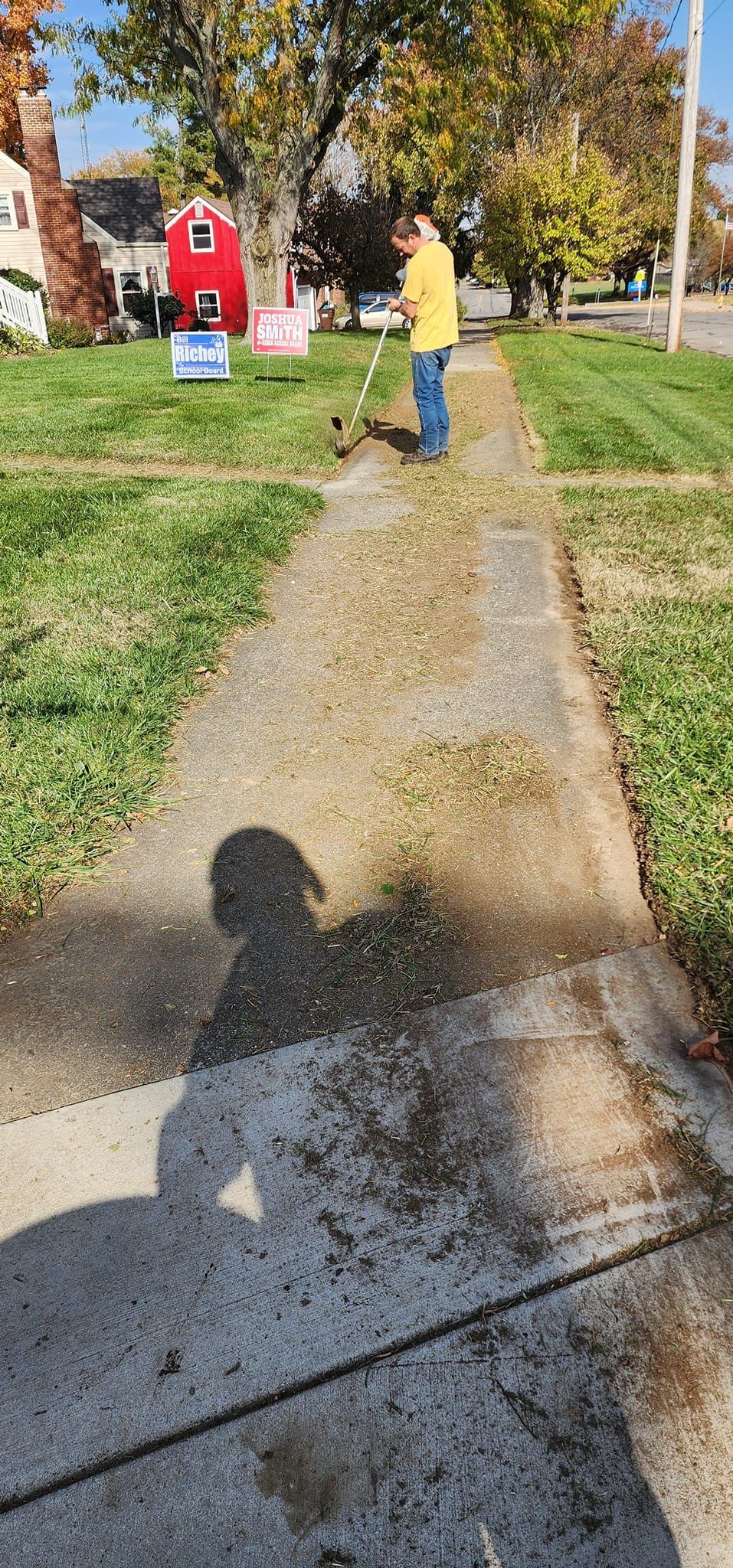 A person is standing on a sidewalk next to a grassy field.