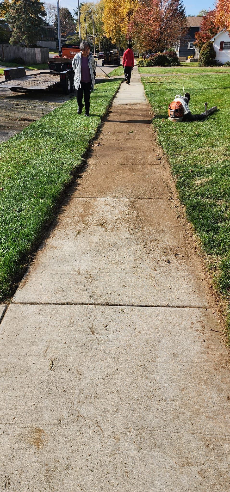 A person is walking down a sidewalk next to a grassy field.