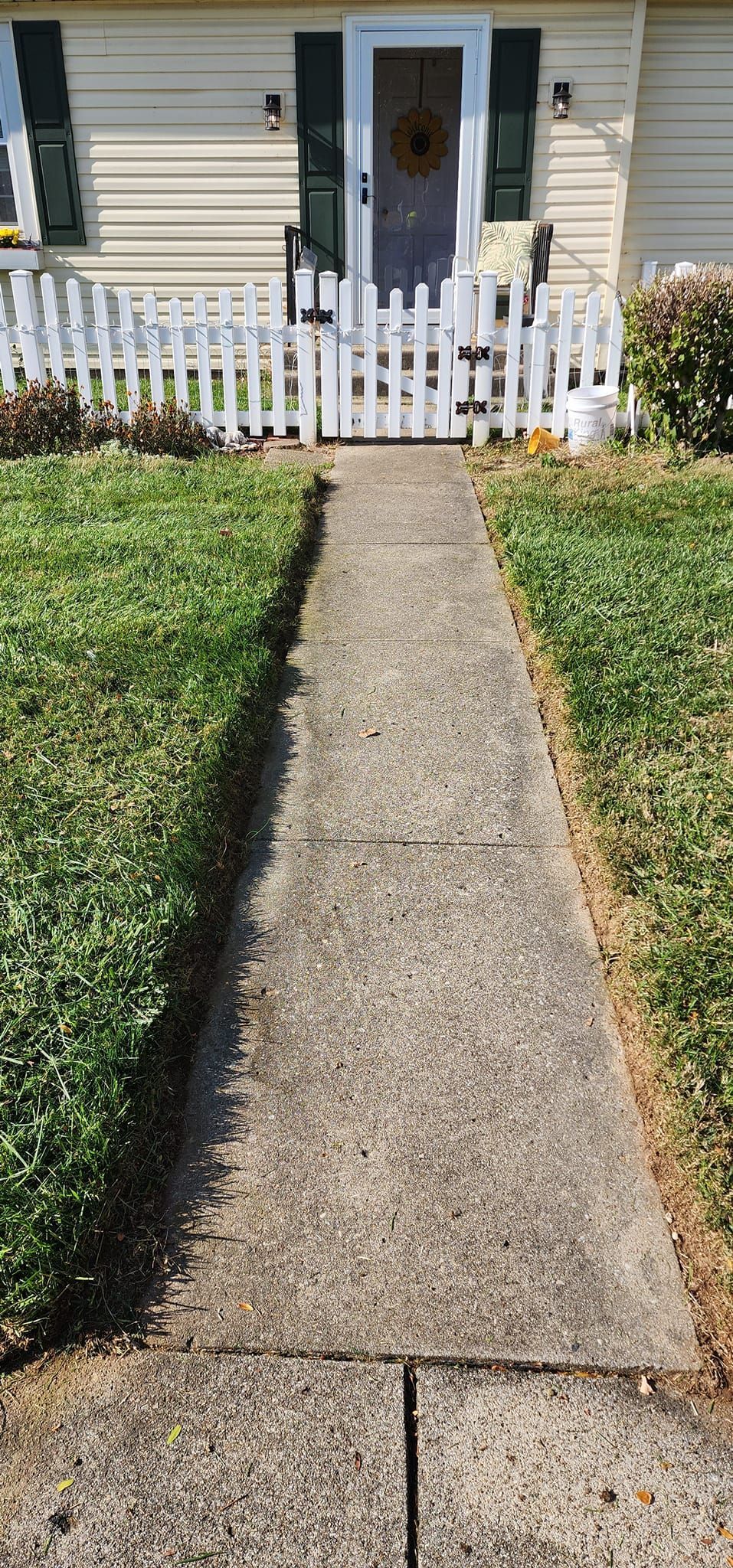 A concrete walkway leading to a house with a white picket fence.