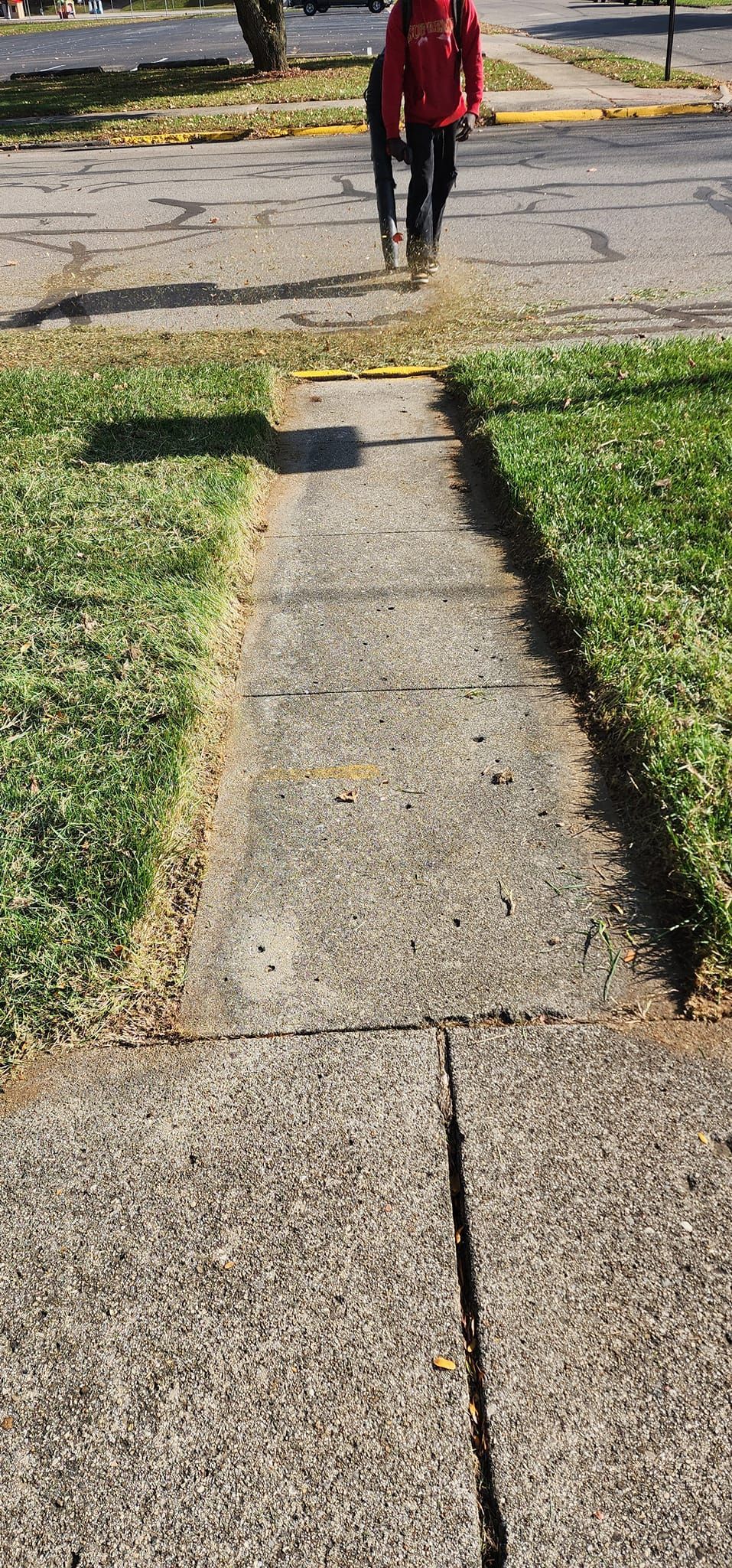 A person is walking down a sidewalk next to a grassy area.