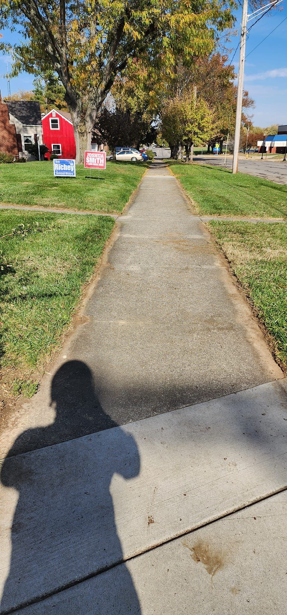 A person is walking down a sidewalk next to a red barn.