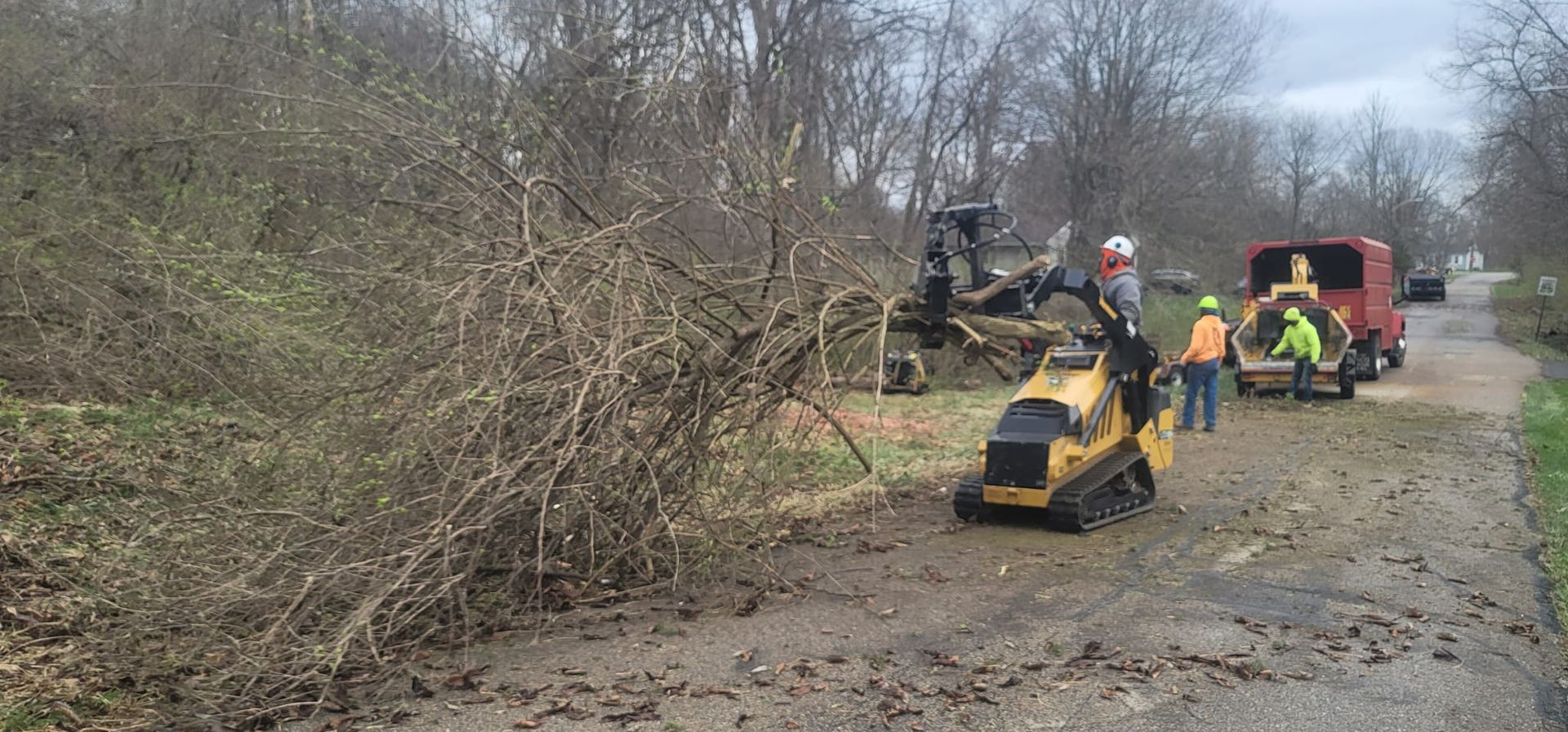 A group of people are working on a tree stump grinder on a dirt road.