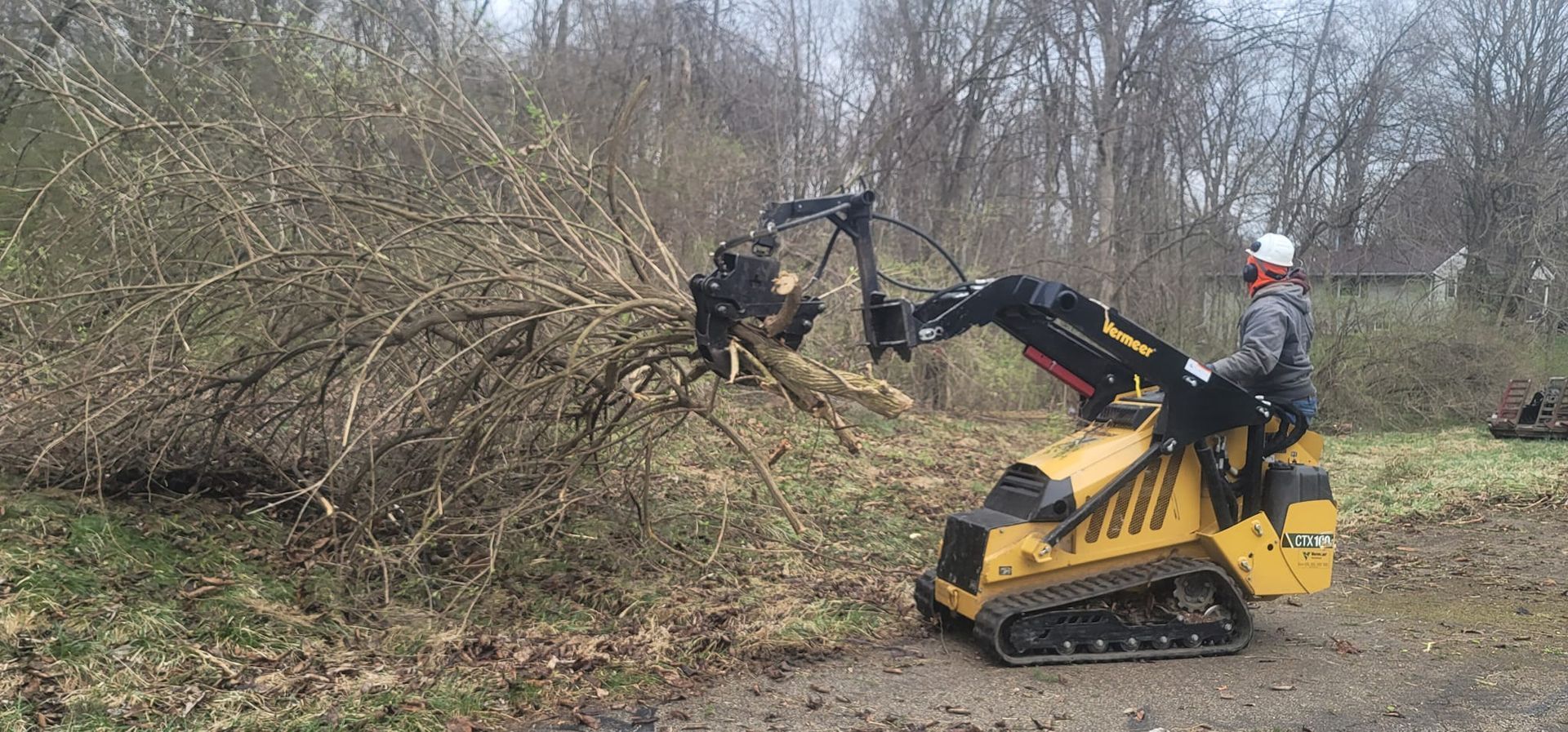 A man is driving a small yellow tractor through a forest.