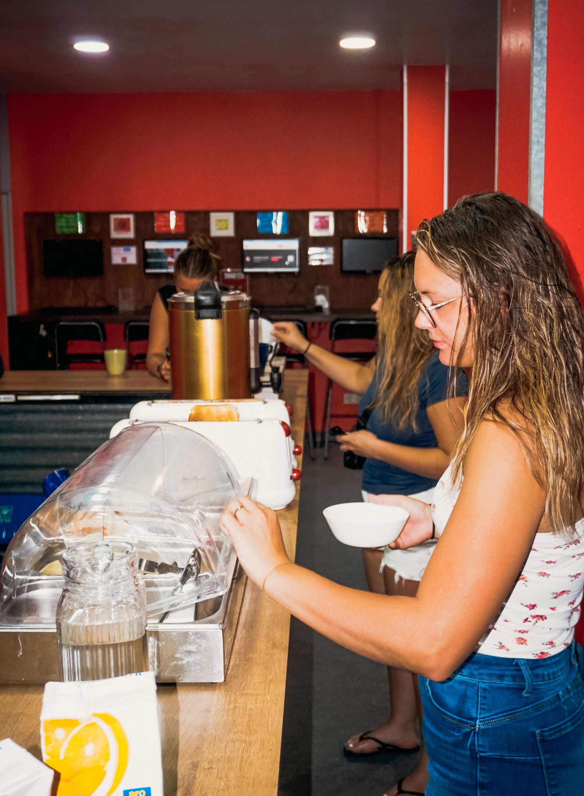 Tres mujeres en un bufé, sirviendo comida. Una sostiene un tazón. Interior rojo y blanco.