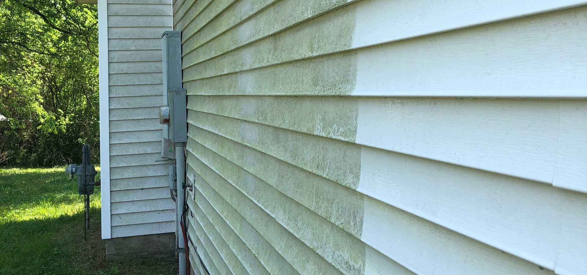 Siding of a house being pressure washed, with a visible difference in cleanliness.