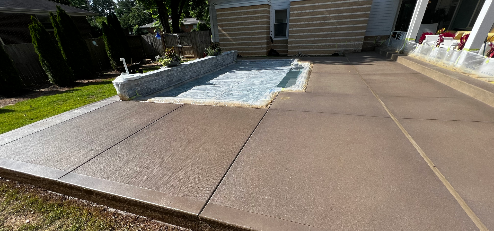 Person cleaning a paved patio with a hose, near a plant.