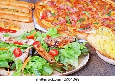 Pizza, salad with grilled chicken, and garlic bread on a wooden table.